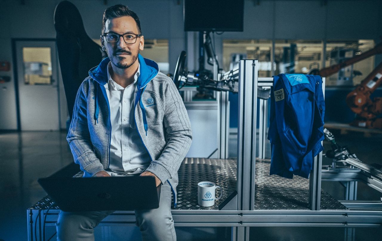 Ein Mann sitzt auf einem Tisch und arbeitet an einem Laptop in einer Werkstatt