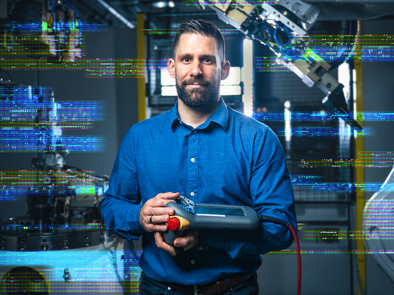 A man is holding a technical device in an industrial environment. The image is partially pixelated.