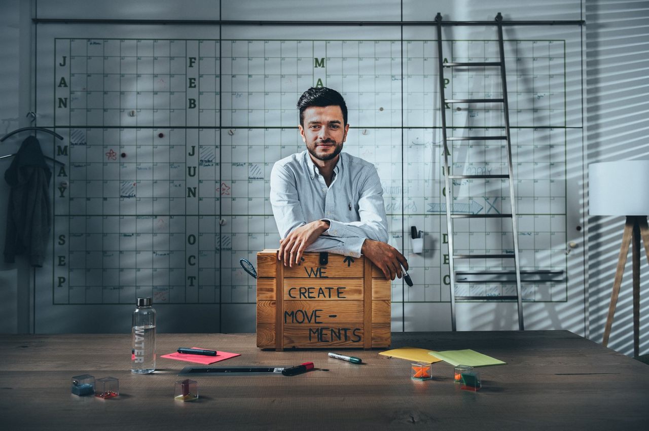 A man is sitting at a desk with a computer. The office is decorated with plants.
