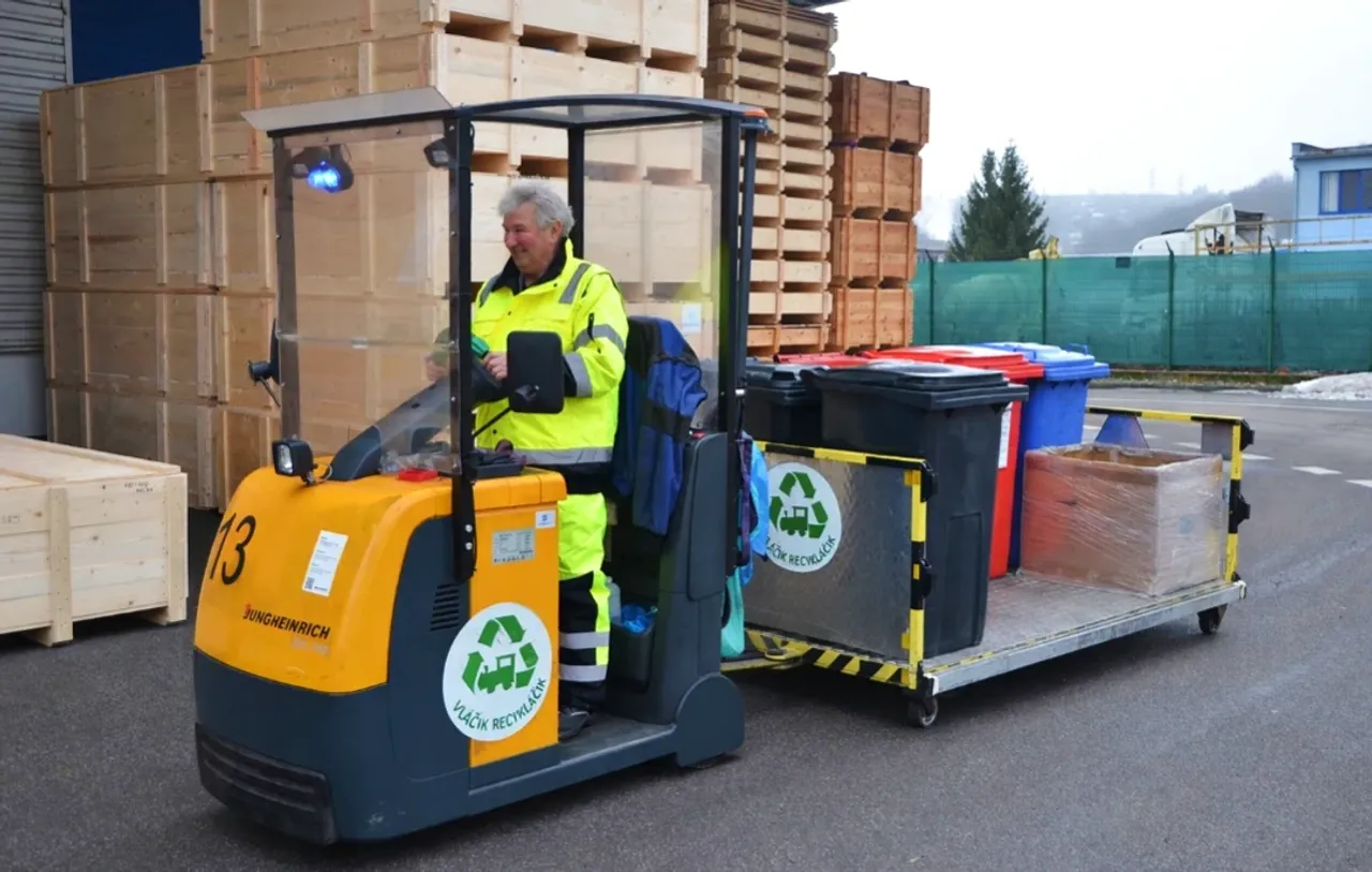 Mann in gelber Arbeitskleidung fährt einen Wagen mit Mülltonnen